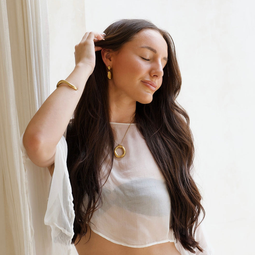 Kyra gold pendant necklace with a polished organic open-centre design and the Capri statement gold stud earrings.