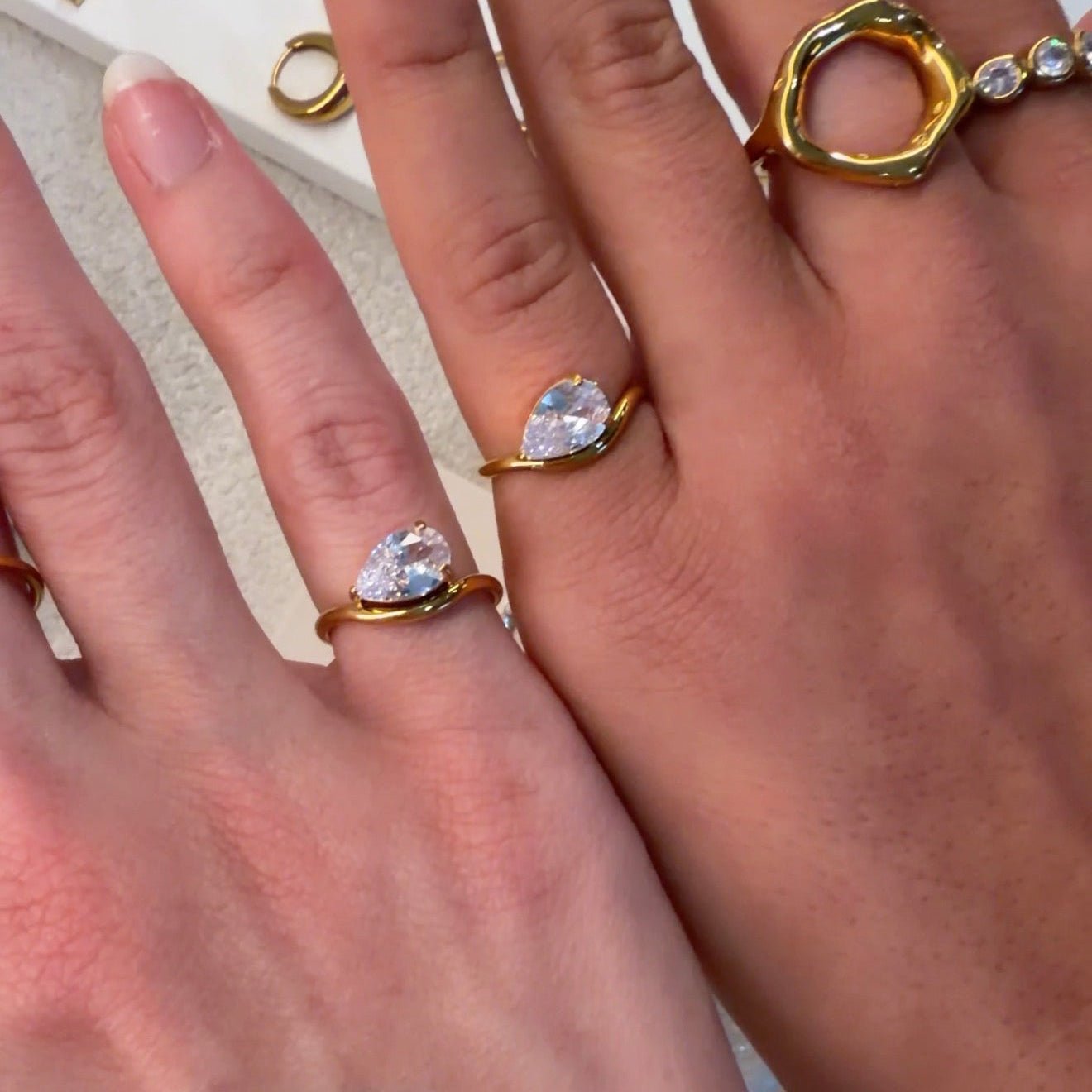 Close-up of hands wearing gold rings with heart-shaped gemstones on a blurred background.